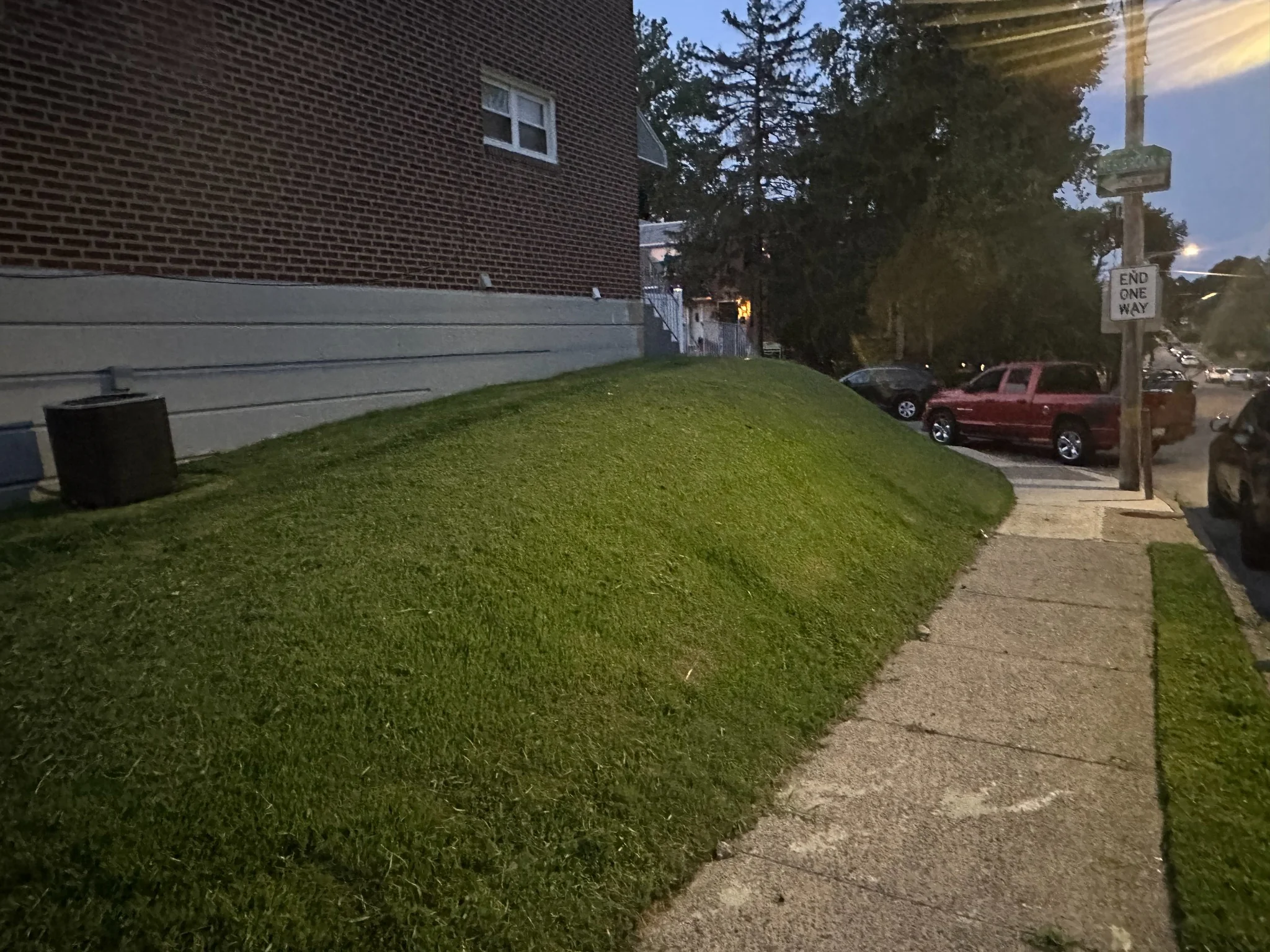 Freshly mowed sloped lawn beside a brick building and sidewalk in a Delaware County neighborhood