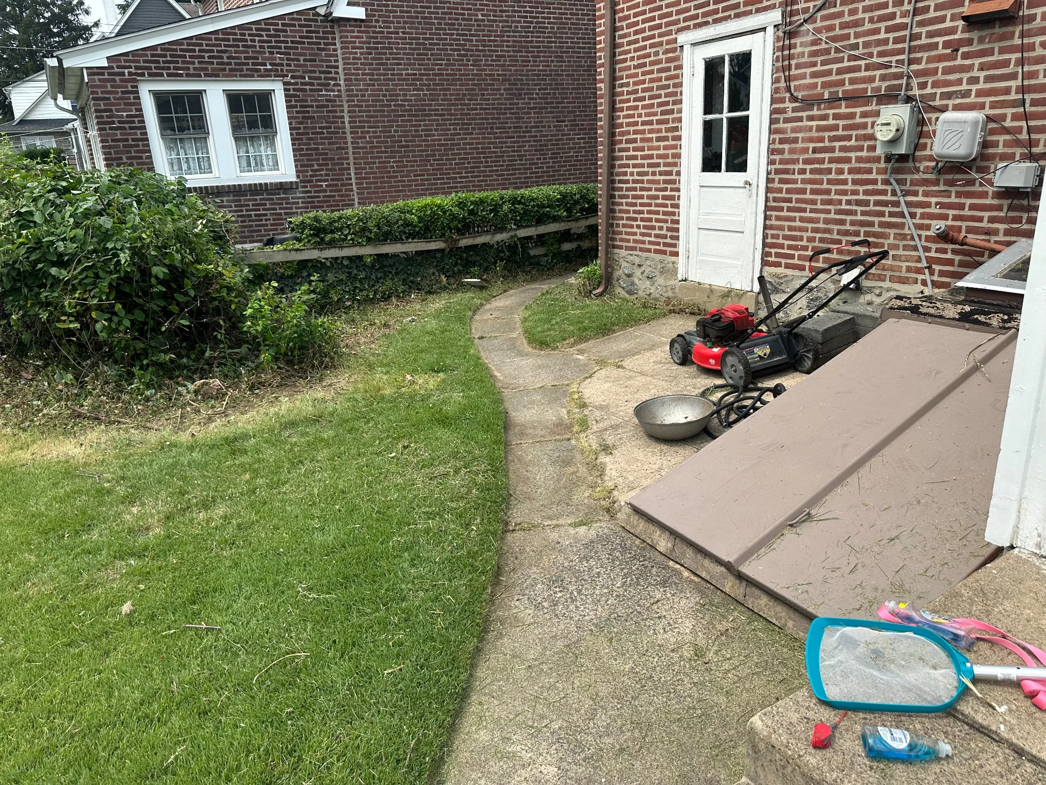Residential lawn maintenance area with freshly cut grass, walkway, hedges, and a lawn mower beside a brick home