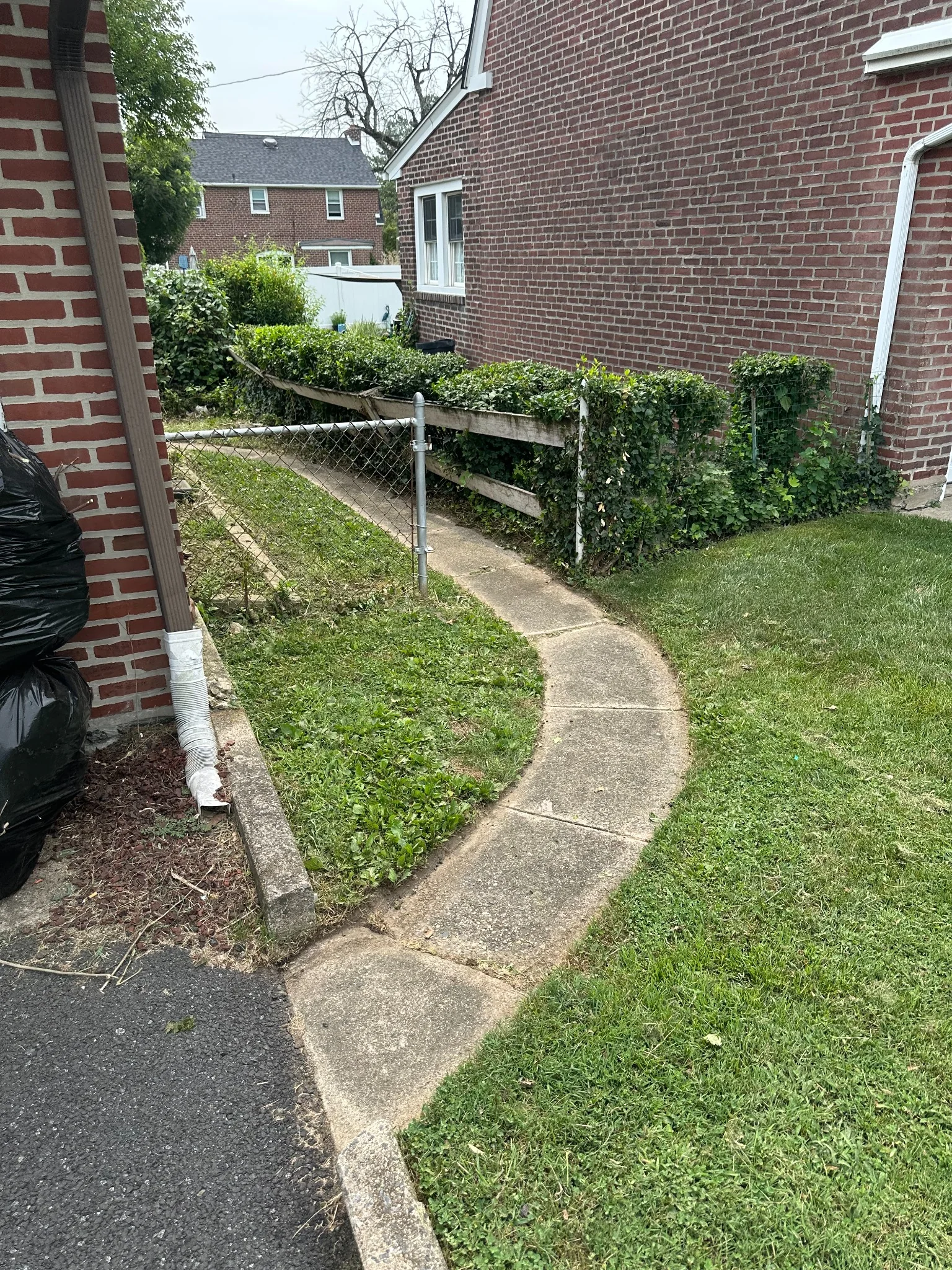 Freshly trimmed side yard with lawn, hedges, and a concrete walkway beside a brick home in Drexel Hill